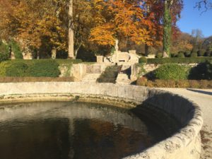 Ein Wasserbassain am Ende des Parks. Es wird durch einen Bach gespeisst, der am hinteren Ende über eine gemauerte Treppe herabfällt. Auf der Wiese darüber stehen Laubbäume in gelb, rot und braun