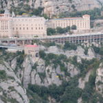 Man sieht das eindrucksvolle Benediktinerkloster Montserrat von einem gegenüberliegenden Felsvorsprung