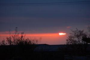 Die größtenteils durch Wolken verdeckte Sonne lässt den Abendhimmel rot orange leuchten.