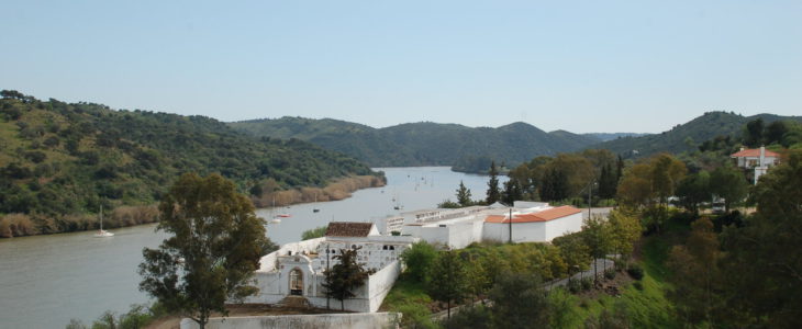 im Vordergrund einige weiß getünchte Gebäude am Flussufer des Guadiana